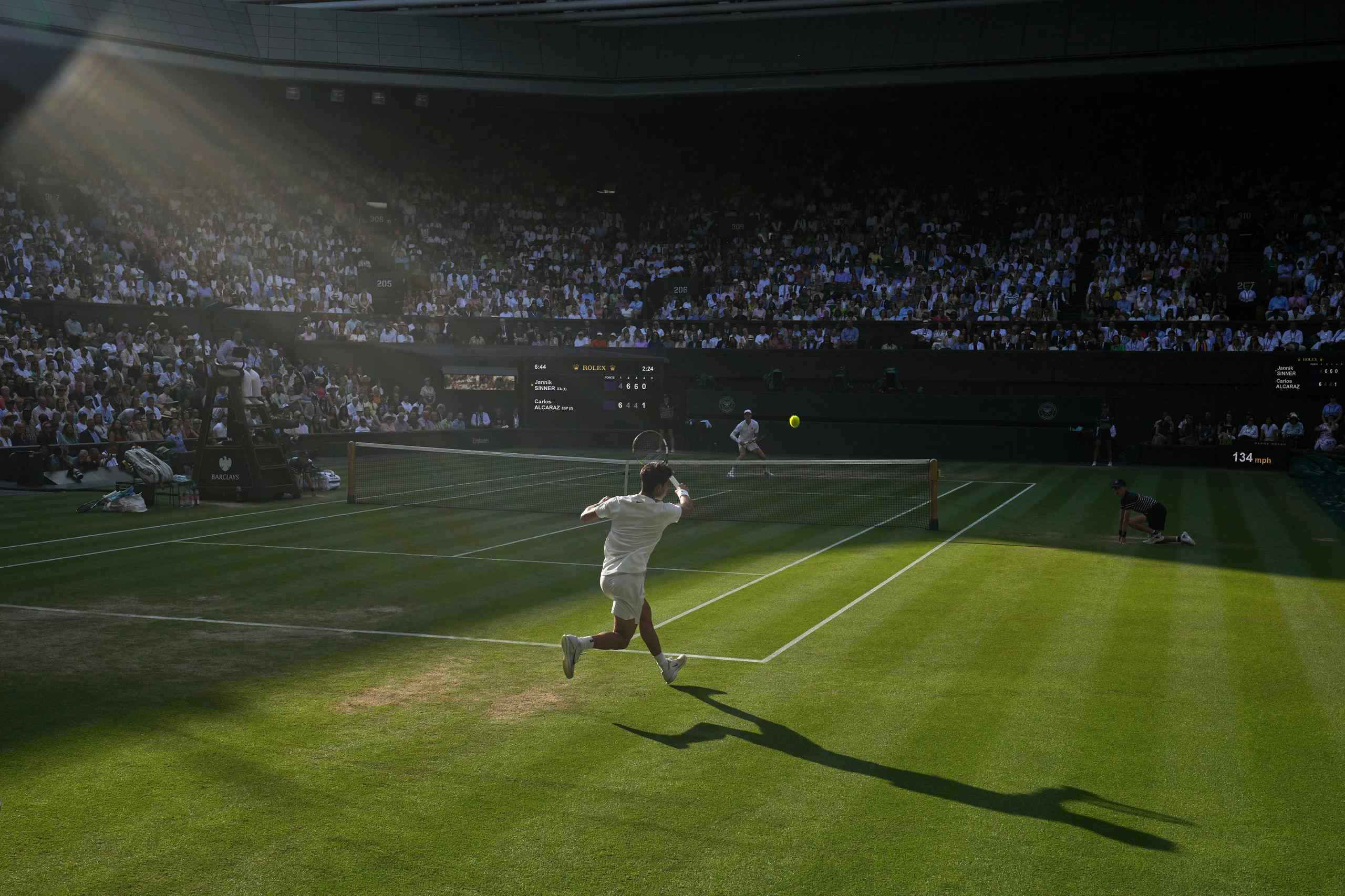 A man swings a Tennis racket at the center of a packed stadium.